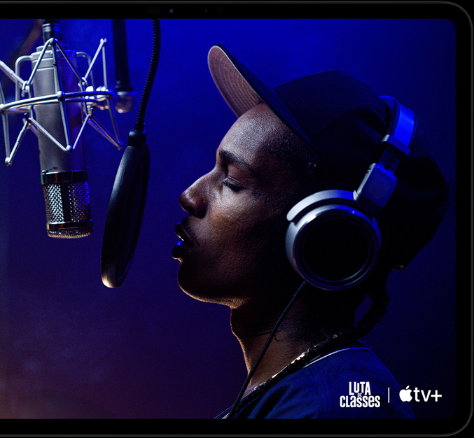 Parte da frente do iPad Pro preto-espacial na horizontal, tela com borda preta mostrando uma cena do filme original do Apple TV Plus, Highest 2 Lowest, com ASAP Rocky interpretando Yung Felon e cantando rap ao microfone