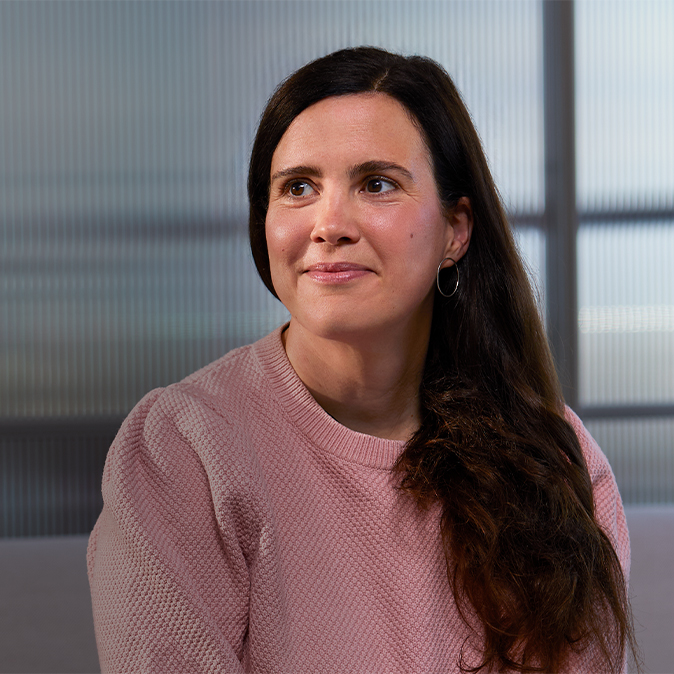 Lucie sitter framför en glasvägg inomhus och ler och tittar åt höger.