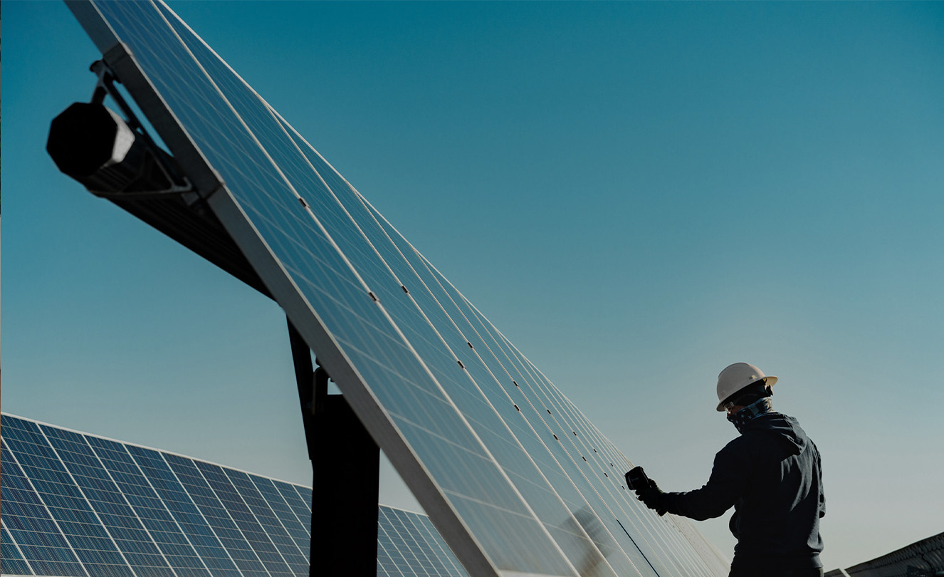 Ein Mann mit Schutzhelm arbeitet im Freien an einem grossen Solarmodul. 