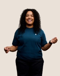 Portrait d’un membre de l’équipe Apple Retail souriant, avec de longs cheveux bouclés de couleur foncée.