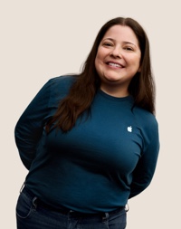 Portrait d’un membre de l’équipe Apple Retail souriant, avec de longs cheveux de couleur foncée.