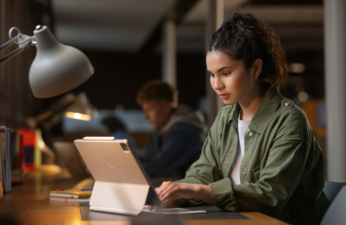 Een student aan een bureau in een studieruimte die op iPad typt met Magic Keyboard, om de veelzijdigheid van Apple devices te demonstreren