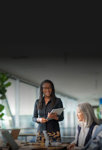 Een universitair medewerker met een iPad die een presentatie geeft, collega’s met opengeklapte MacBooks luisteren aandachtig