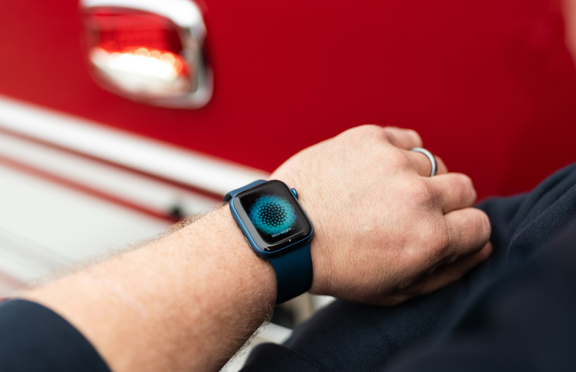 An arm wearing an Apple&nbsp;Watch displays the message: Now inhale, with a fire engine nearby