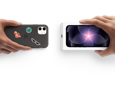 Two hands side-by-side, hand holding iPhone 11 in Silicone Case with stickers on back exterior, trade-in, with hand holding new iPhone 17e box