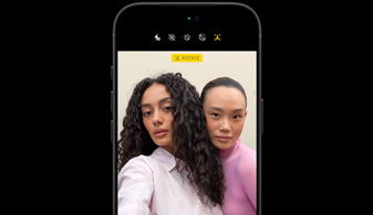 Pohled zepředu na černý iPhone 18 Pro, na kterém funkce sledování obličejů zaostřuje na dvě osoby, jde o ukázku fungování přední Center Stage kamery
