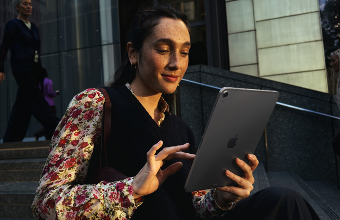 Eine Person sitzt auf Stufen vor einem großen Gebäude und nutzt ein 11 Zoll iPad Air in Space Grau mit nahtloser WLAN Verbindung während der Datenübertragung