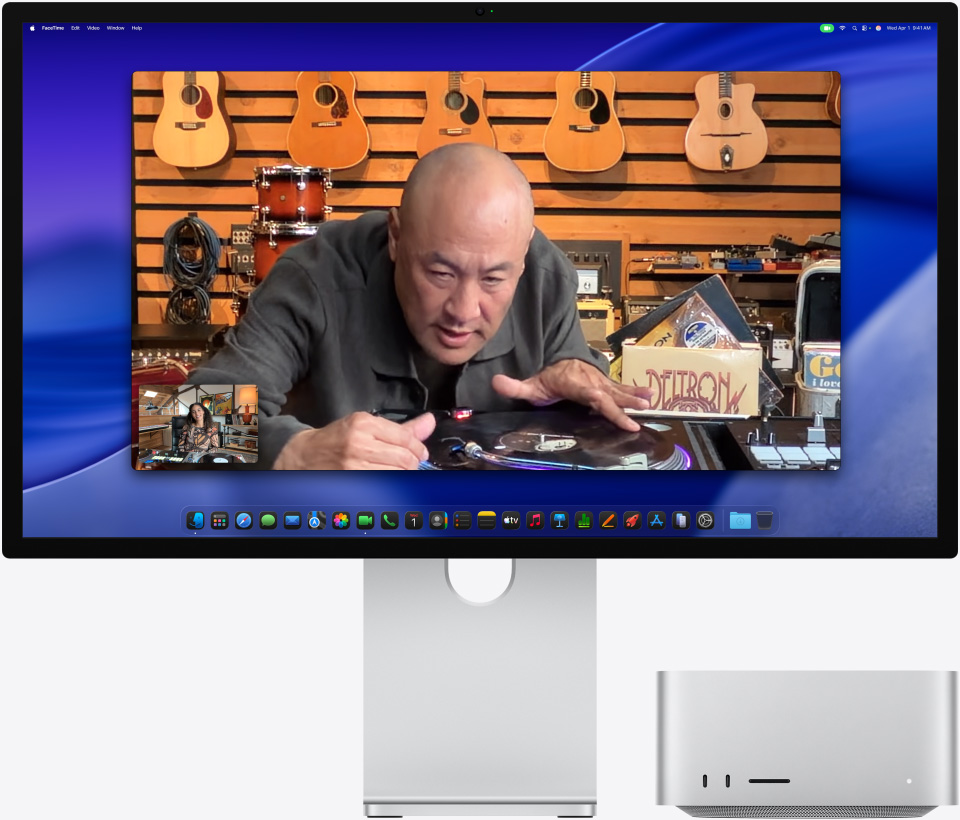 Durante uma chamada de vídeo no Studio Display XDR com o Mac Studio embaixo, uma pessoa em uma loja de música observa um toca-discos