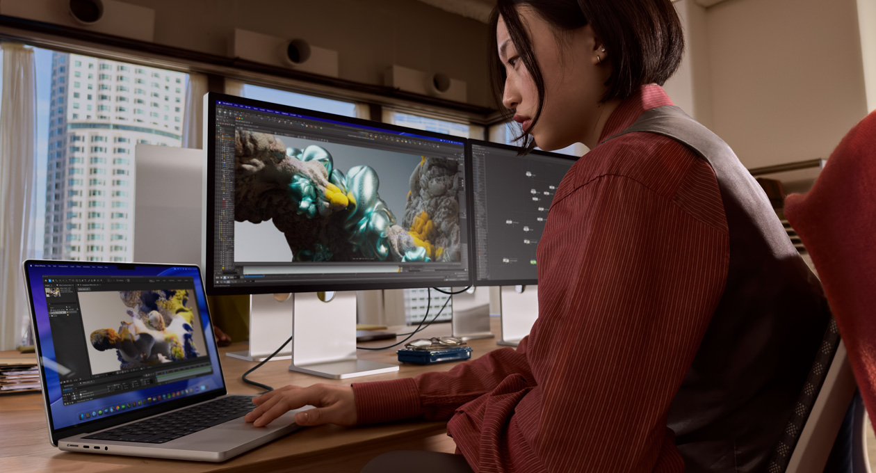 一個人在辦公室的場景中使用 MacBook 筆電進行工作，筆電是透過 Thunderbolt 5 埠連接至 Studio Display XDR